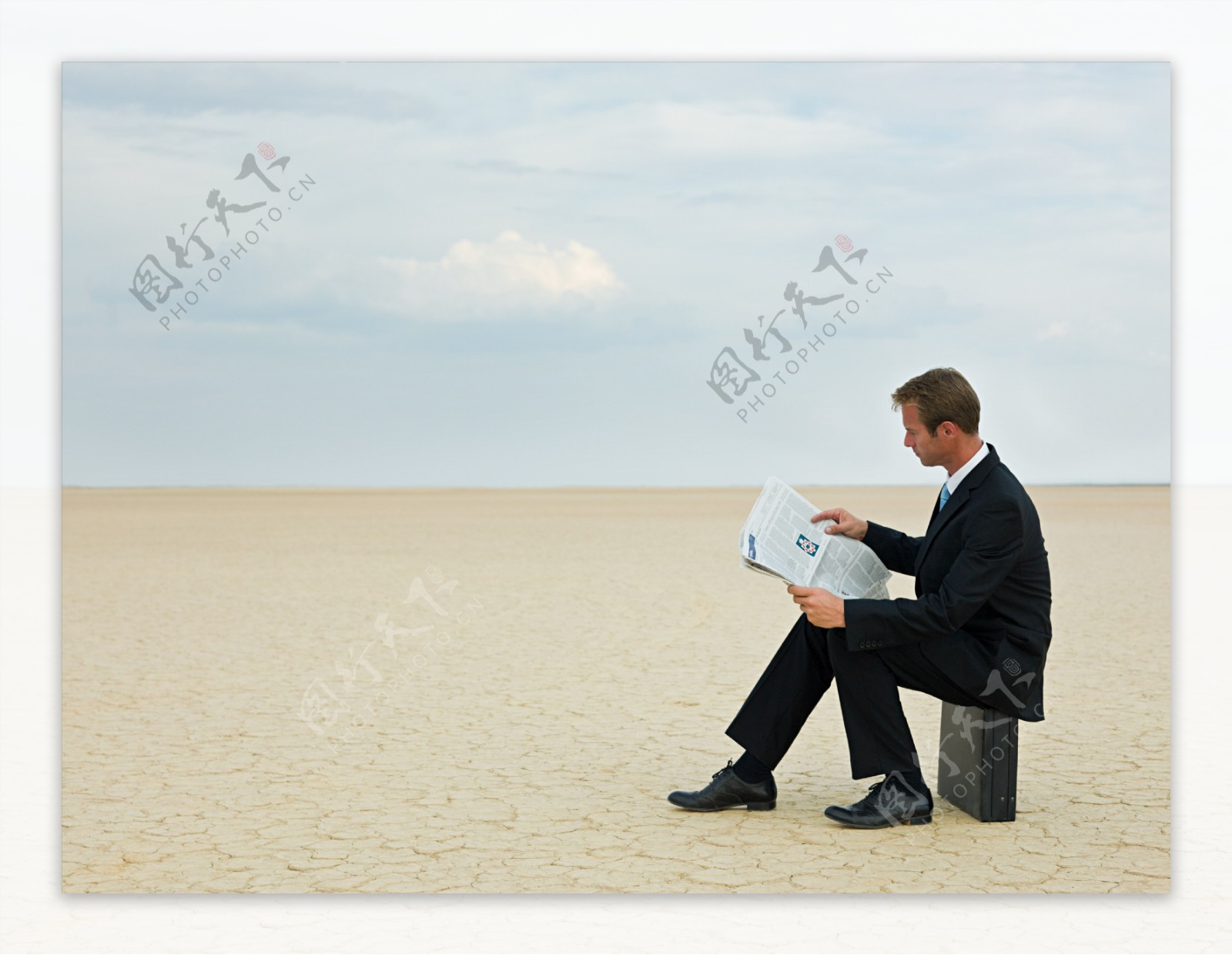 坐在裂缝土地上看报纸外国商业男人图片